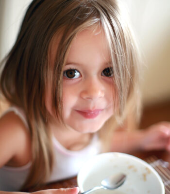 Happy four years old girl has breakfast and smiles at the camera.