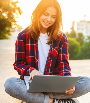 Cheerful young girl using laptop while sitting on a city street