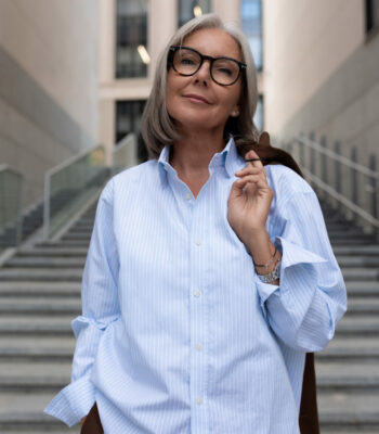 portrait of a model slender gray-haired woman of mature years dressed in a light blue shirt standing against the background of the entrance to the business center.