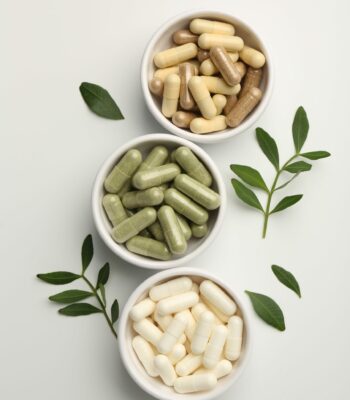 Different vitamin capsules in bowls and leaves on white background, flat lay Different vitamin capsules in bowls and leaves on white background, flat lay